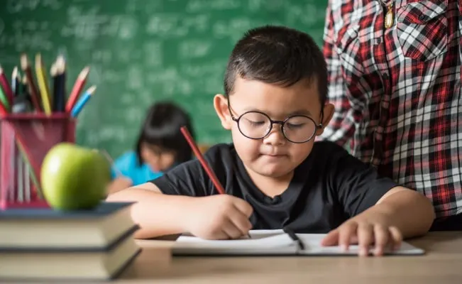 Young student with glasses focused on writing.