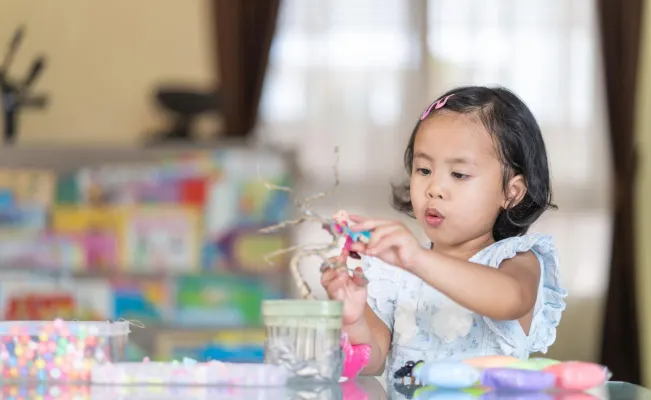 Little girl focused on a craft project with colorful materials on the table.